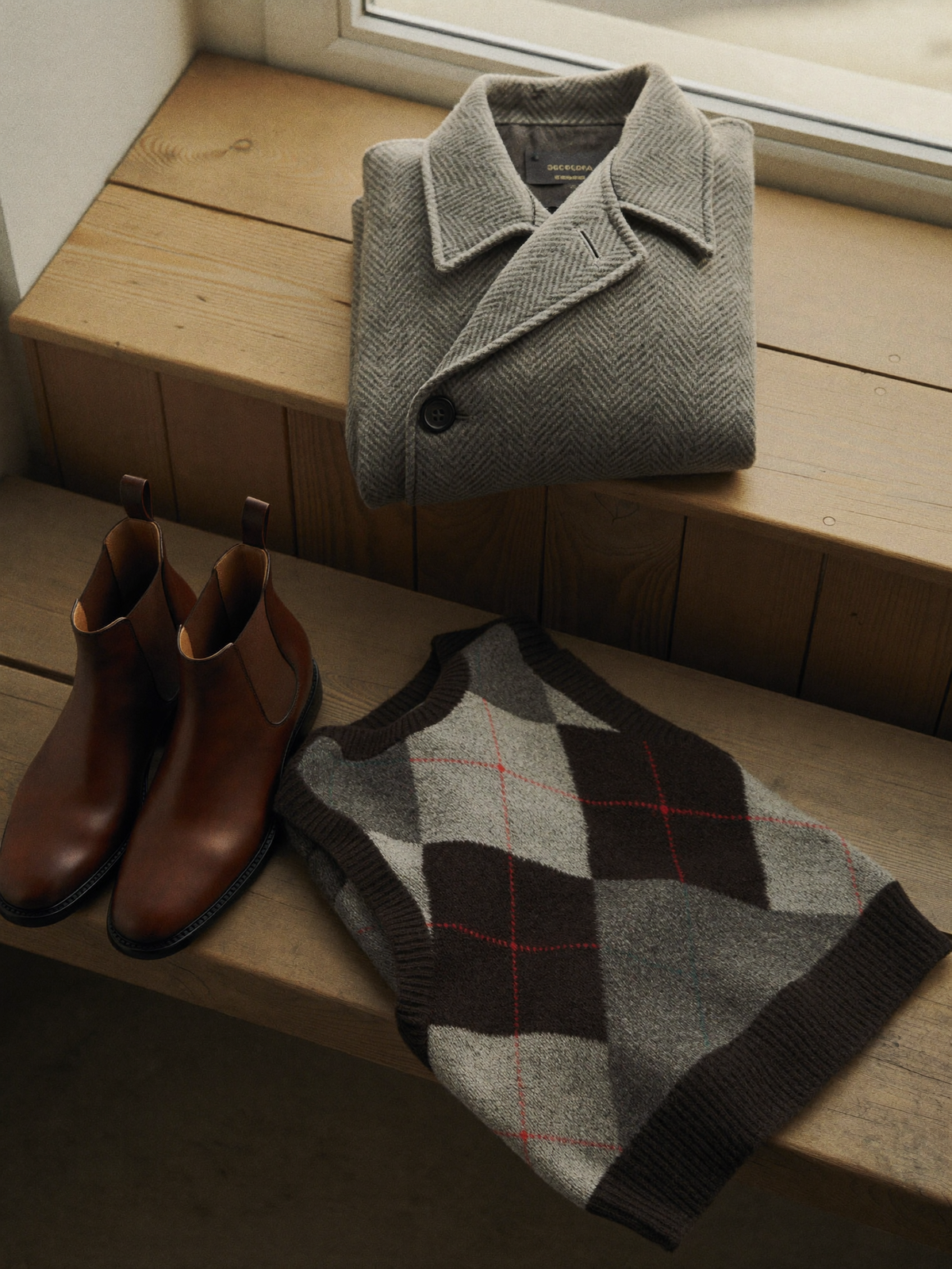 Herringbone coat, Chelsea boots and argyle vest on a wooden bench